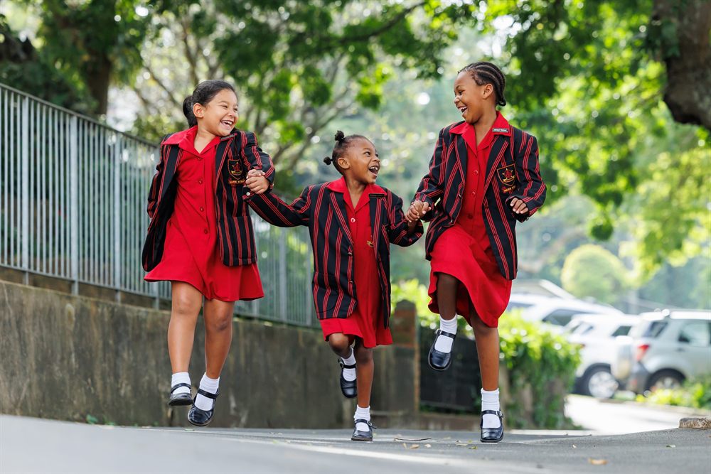 Three Senior Primary girls in blazers skipping hand in hand