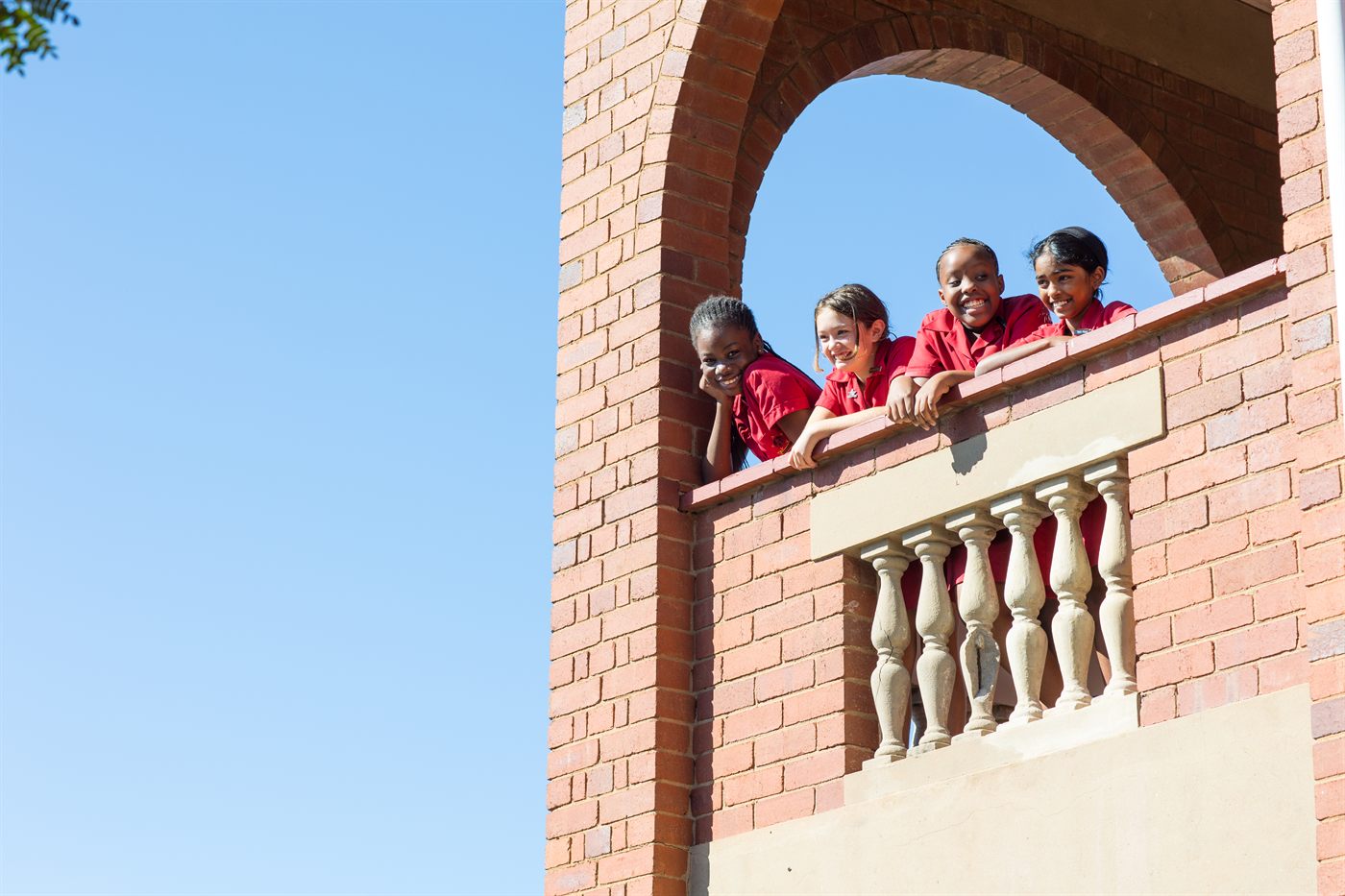 Maris Stella girls smiling down from a brick archway against a blue sky